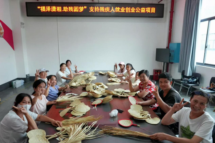 （图为：残疾工人们在制作福彩定制手工编织扇）