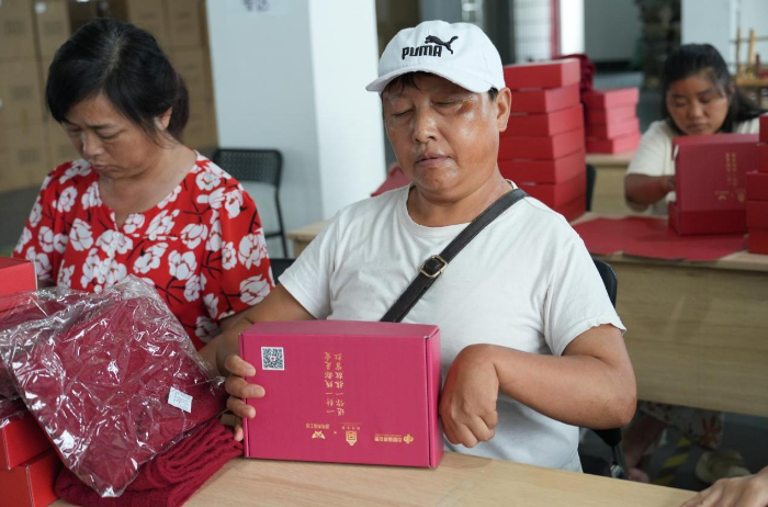 （图为：残疾工人们制作福彩定制手工故宫红-经纬纹款围巾）